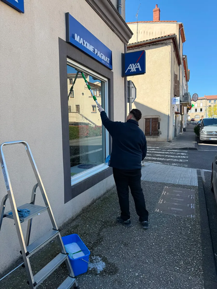 Un intervenant nettoie la vitrine d'une agence avec une perche et une échelle
